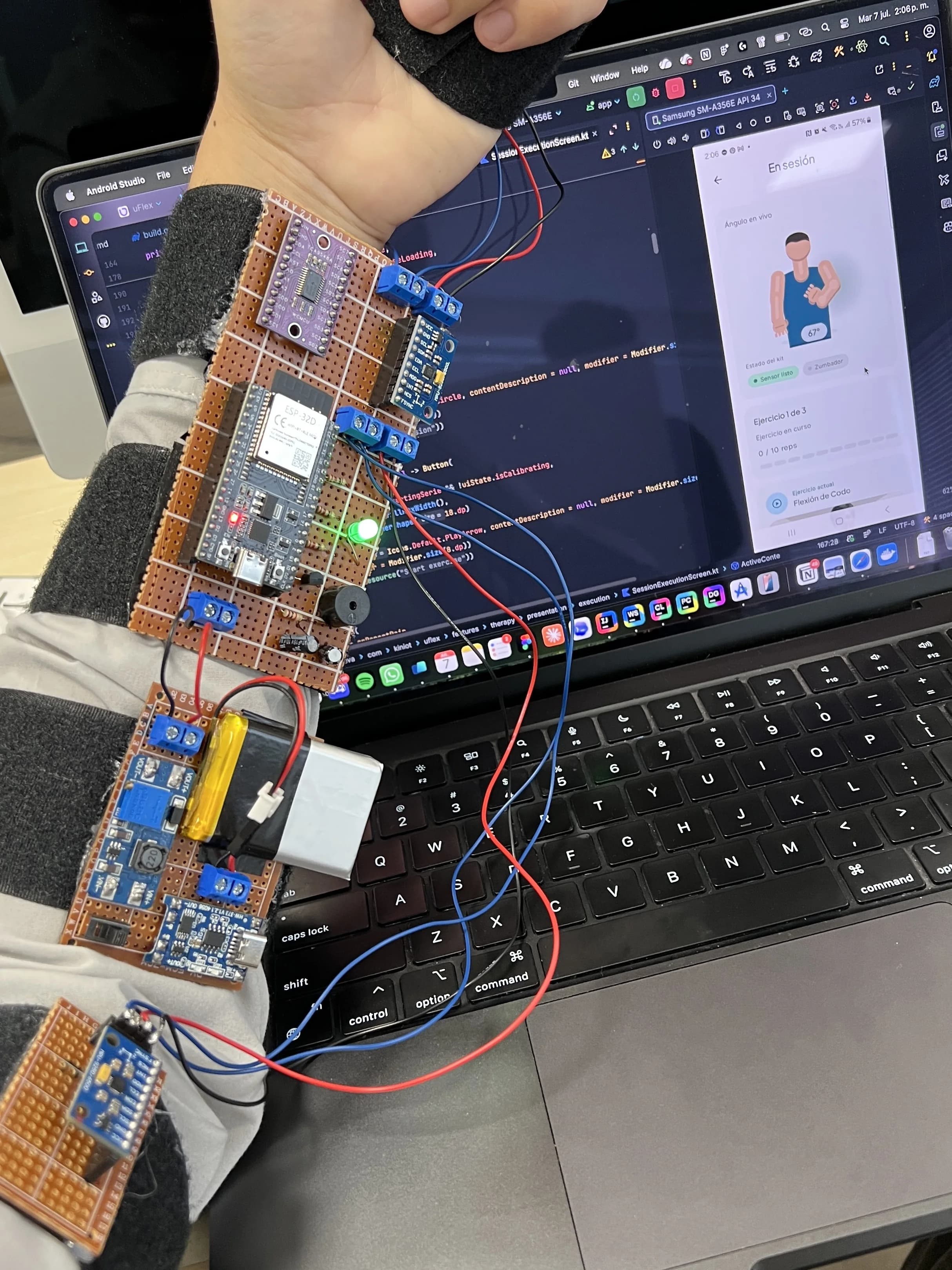 Wearable de uFlex sobre el antebrazo: placa ESP32, sensores IMU y batería cableados, con la app en ejecución en una laptop detrás.